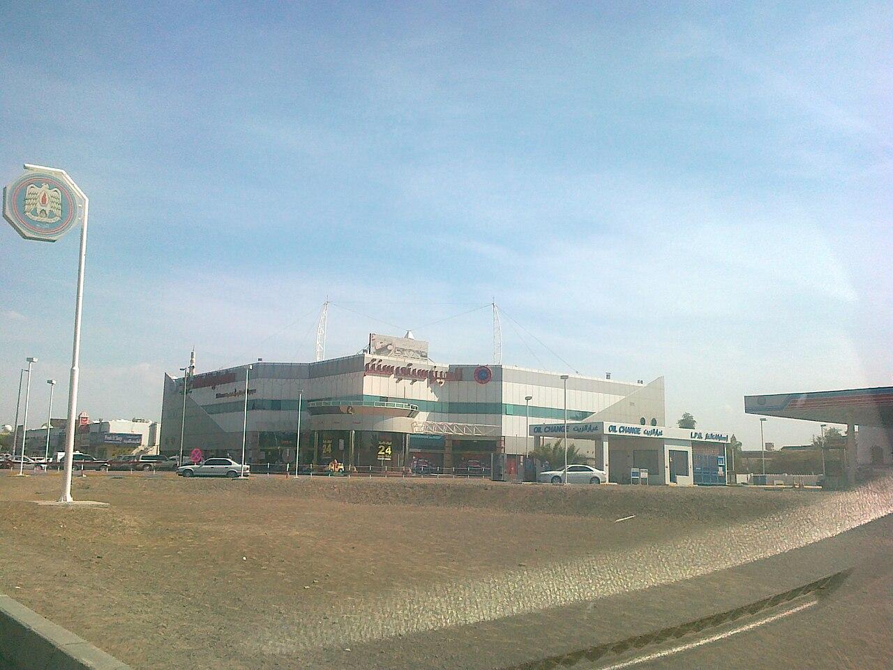 Al Ain International Airport terminal building exterior with UAE emblem signpost