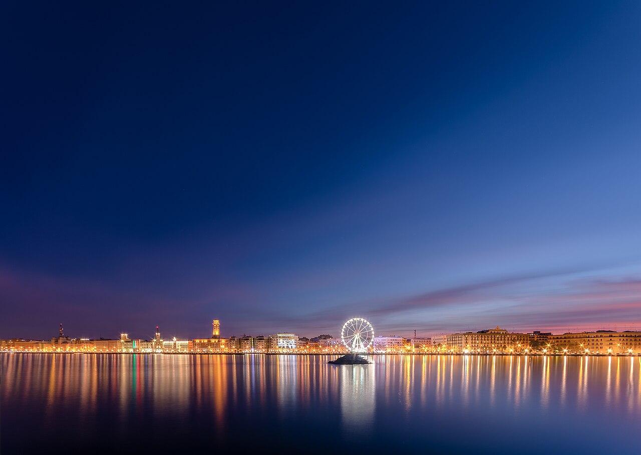 Bari city waterfront at dusk with illuminated Ferris wheel reflected in the sea